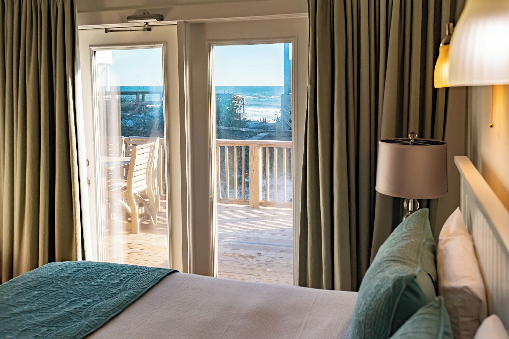 A hotel room with a bed, a lamp, and a view of the ocean through a sliding door.