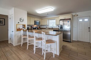 Eine moderne Küche mit weißen Schränken, einer Granit-Arbeitsplatte, Edelstahlgeräten und einer Frühstückstresen mit weißen Stühlen.