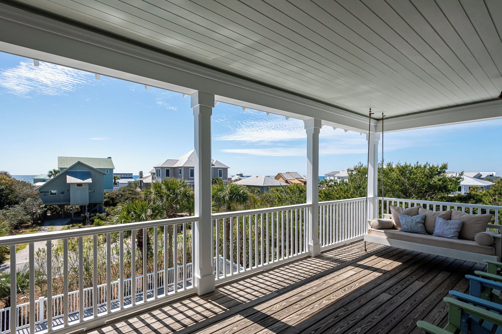 A covered porch with a wooden deck, white railings, and a cushioned seating area.