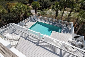 Ein rechteckiger Pool mit weißem Deck und Geländern, umgeben von Palmen und anderer Vegetation.