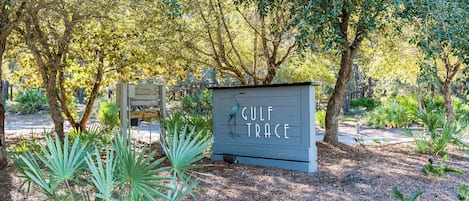 Uma placa de madeira com a inscrição 'GULF TRACE', rodeada por árvores e plantas.