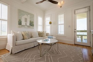 Uma sala de estar espaçosa com um sofá branco, uma mesa de centro e uma pintura na parede.