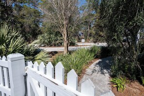 A pathway surrounded by various plants and trees, leading to a building with a white picket fence. - Private Pool, Short Walk to Beach- Milly Mae's Cottage by Royal Destinations (Santa Rosa Beach)