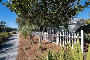 A residential street with a white picket fence, a sidewalk, and a house with a covered porch. - Across From Beach, Steps From Seaside- Mimi's Cottage by Royal Destinations (Santa Rosa Beach)