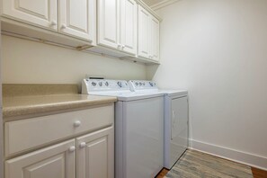A laundry area with a washer and dryer, beige countertop, white cabinets, and a patterned rug. - Across From Beach, Steps From Seaside- Mimi's Cottage by Royal Destinations (Santa Rosa Beach)