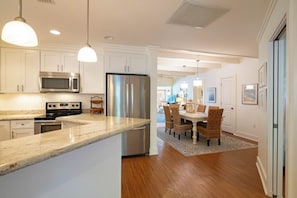 A modern kitchen with stainless steel appliances, a marble countertop, and a dining area with wicker chairs. - Across From Beach, Steps From Seaside- Mimi's Cottage by Royal Destinations (Santa Rosa Beach)
