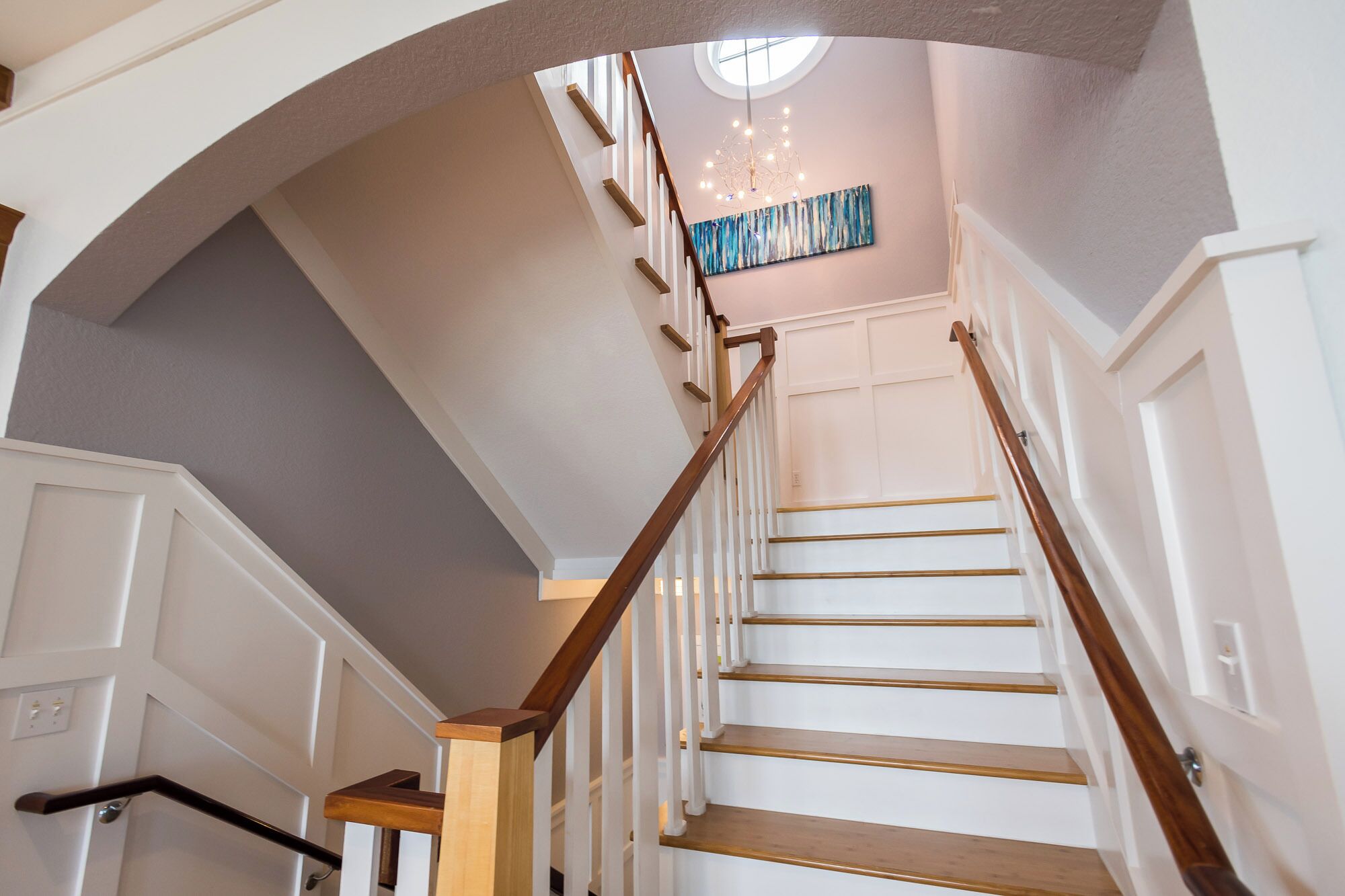 A staircase with wooden handrails and white walls, leading to a landing with a ceiling light fixture.