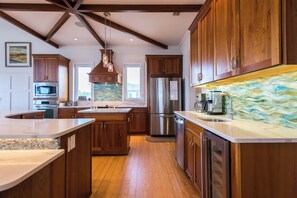 Cocina moderna con alacenas de madera, electrodomésticos de acero inoxidable, una isla grande y vistas al exterior.