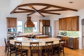 A modern kitchen with wooden cabinets, stainless steel appliances, a large island with bar stools, and a unique ceiling design. - Gulf Views, Steps From Beach, Elevator- Mimosa Mornings by Royal Destinations (Santa Rosa Beach)