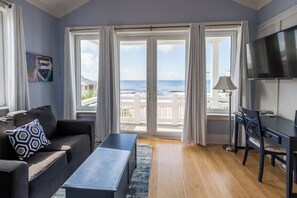 Una habitación con sofá, mesa de centro, televisor y vistas al océano a través de amplios ventanales correderas.