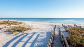 Ein Strand mit einer Holzpromenade, die zum Wasser führt, Sanddünen und einem klaren Himmel.