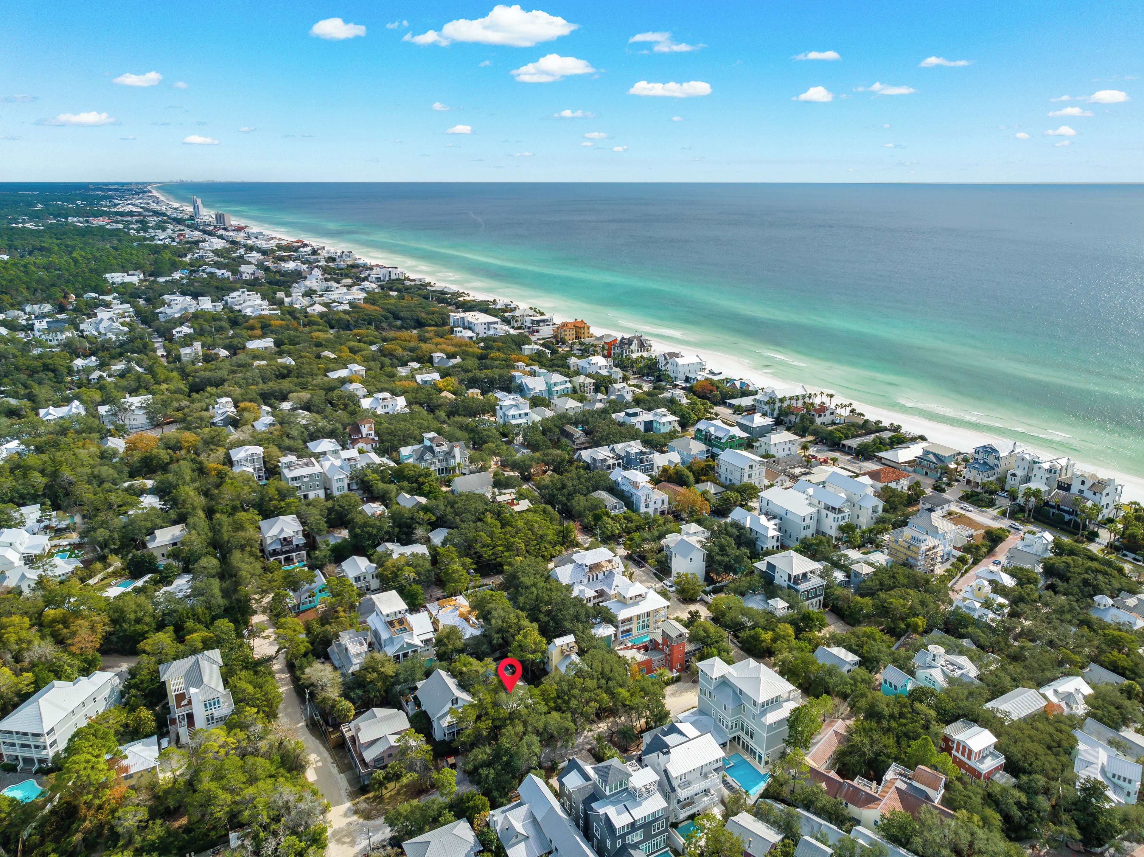 An aerial view of a coastal residential area with houses, trees, and a beach.