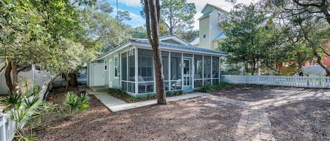 A small house with a screened porch, a fenced yard, and a brick pathway.