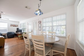A dining area with a round table and white chairs, large windows with blinds, and a ceiling fan. - Pet Friendly with Pool, Near Beach & Seaside- Moondance by Royal Destinations (Santa Rosa Beach)