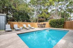Une piscine rectangulaire avec une terrasse en bois, entourée d’une clôture en bois et d’arbres.