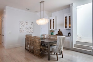 A dining area with a dark wooden table and wicker chairs, a chandelier, and a white cabinet with glass doors. - Private Pool, Steps From Beach Access- Ocho Cinco by Royal Destinations (Santa Rosa Beach)