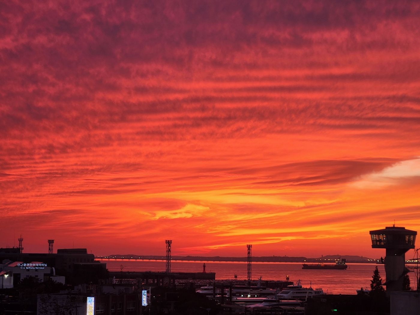 A sunset over a harbor with a bridge and buildings in the foreground.