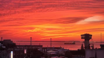 Atardecer sobre un puerto con una torre de control, coches aparcados y edificios en primer plano.
