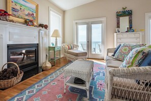 A living room with a fireplace, wicker furniture, a colorful rug, and a view of the sea through the windows. - Gulf Front with Private Beach Access- Port of CAW by Royal Destinations (Santa Rosa Beach)