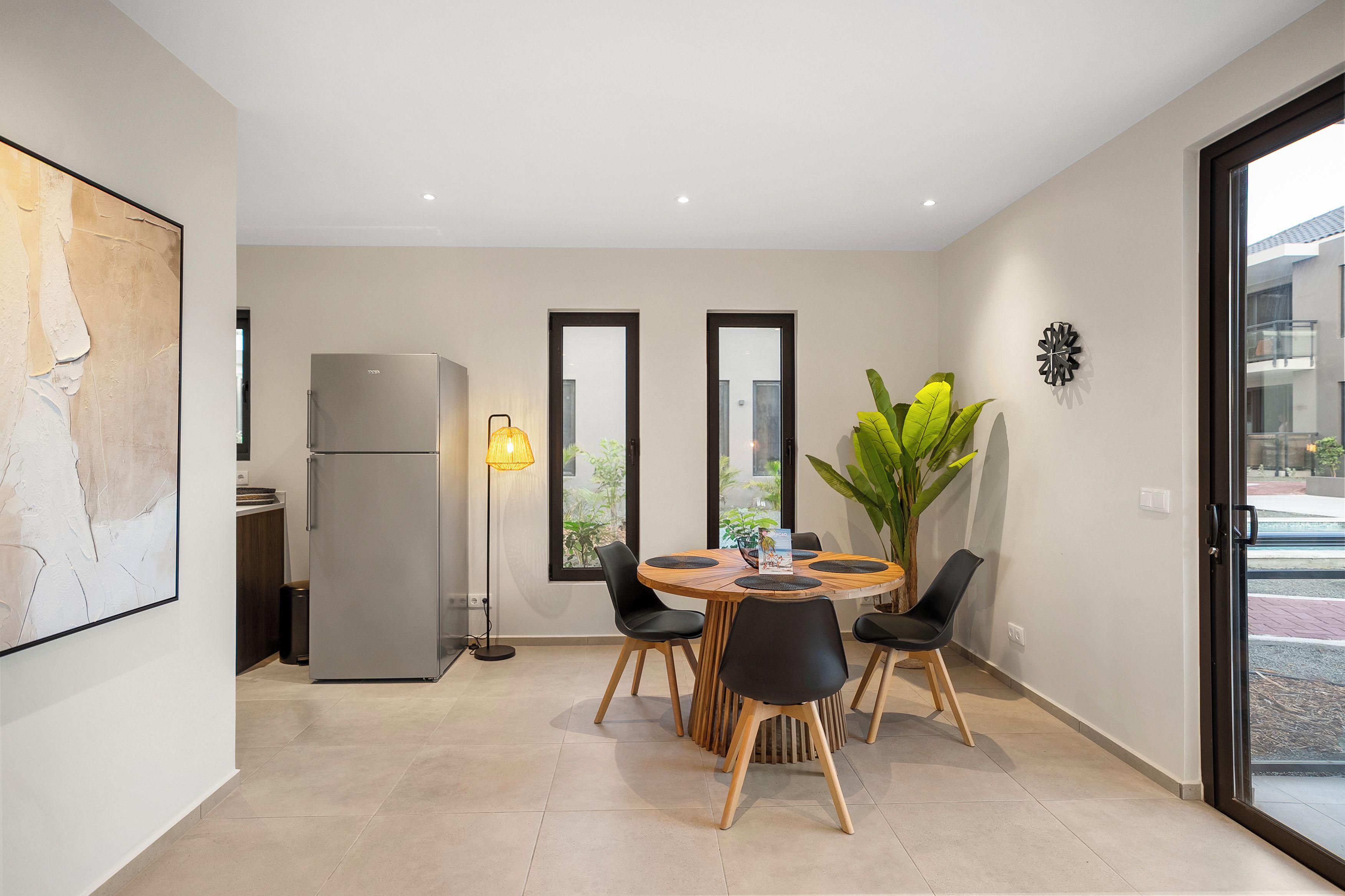 Een moderne eetruimte met een ronde tafel, stoelen, een koelkast en een vloerlamp.