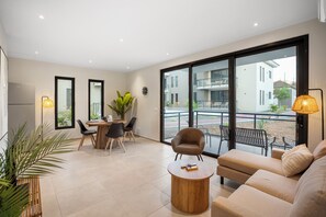 A modern living room with a sofa, a coffee table, and a dining area with chairs and a table. There is a balcony with a view of buildings and a plant. - newly build 12 Luxury 2BR/2BA apartments on gated resort with pool, ideally located near Mambo Beach & Jan Thiel. Fully equipped kitchen, AC in all rooms, private balcony. Perfect for a comfortable and relaxing stay in Curaçao. (Willemstad)