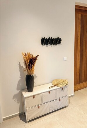 Quarto com um armário branco encostado à parede, um vaso com flores secas e um objeto preto fixado na parede.