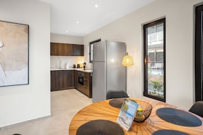 Eine moderne Küche mit dunklen Holzschränken, einem Edelstahlkühlschrank und einem Essbereich mit einem runden Holztisch und schwarzen Stühlen.