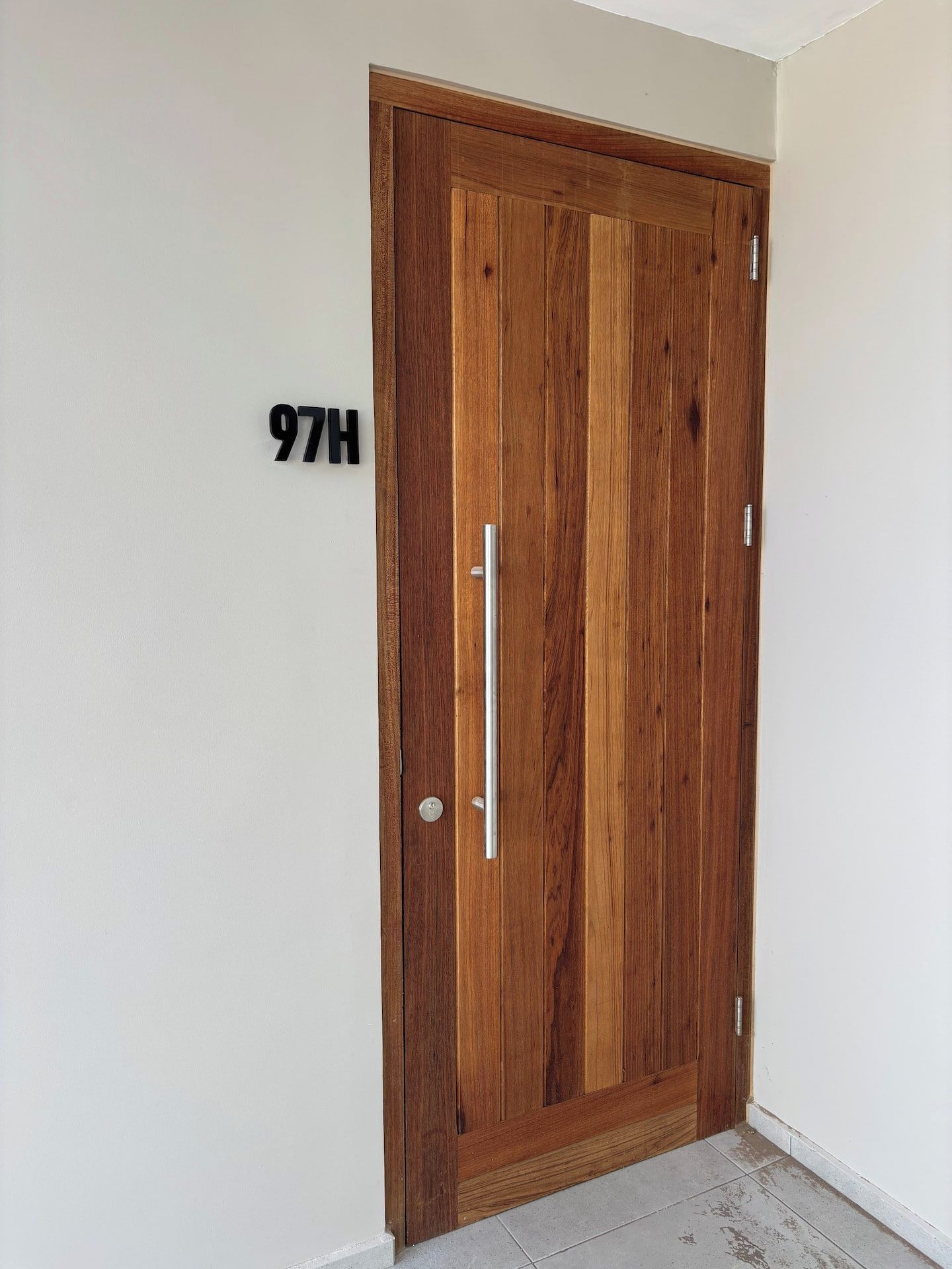 Una puerta de madera con un picaporte y el número '97H' en la pared de al lado.