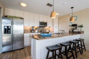 A modern kitchen with a stainless steel refrigerator, a microwave, and a coffee maker. There are wooden stools and a large island with a sink. - Private Pool with Gulf Lake & Park Views- SeaBatical by Royal Destinations (Santa Rosa Beach)