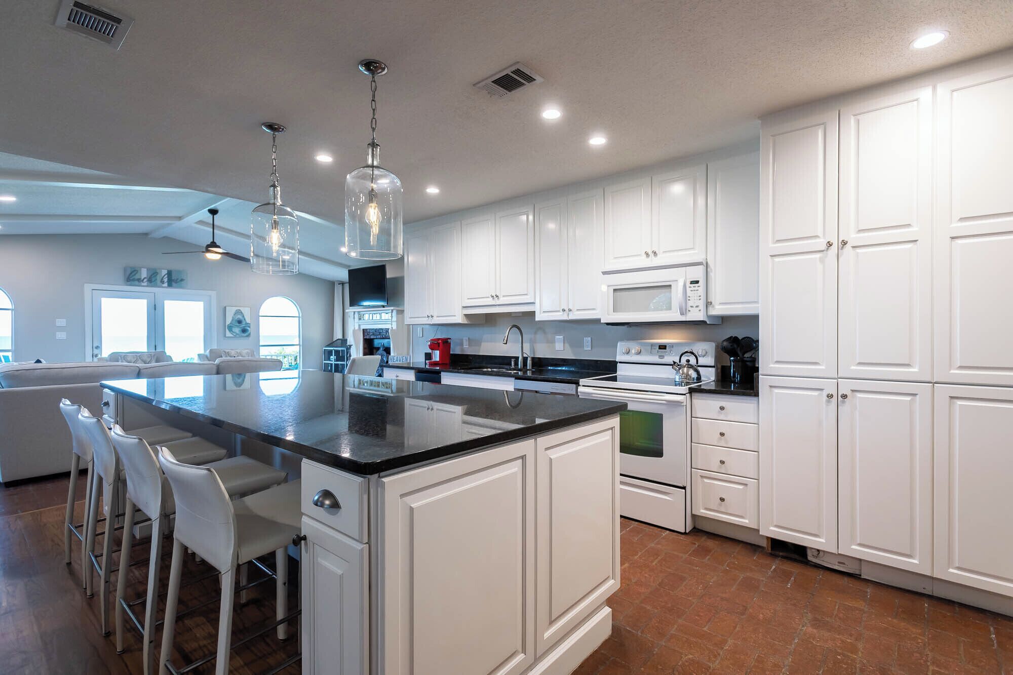 A modern kitchen with white cabinetry, a large island with bar stools, and a flat-screen TV above the counter.
