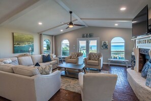 A spacious living room with a high ceiling, a ceiling fan, a fireplace, and a view of the ocean through large windows. - Gulf Front w/ Private Beach Access- Sea Turtle Cottage by Royal Destinations (Santa Rosa Beach)