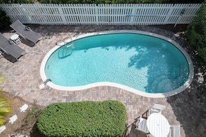 Ein Swimmingpool mit einer Ziegelterrasse, einem weißen Zaun und Gartenmöbeln.