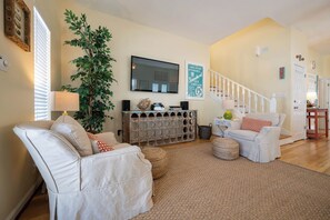 A living room with a sofa, a coffee table, a television, a staircase, and a potted plant.