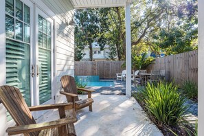 A covered patio with a pool, wooden chairs, and a table. - Private Pool, Steps From Beach & Seaside- Sunday Morning (Santa Rosa Beach)