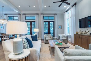 A spacious living room with a high ceiling, large windows, and a ceiling fan. - Private Pool, Steps From Beach & Seaside- Sunday Morning (Santa Rosa Beach)