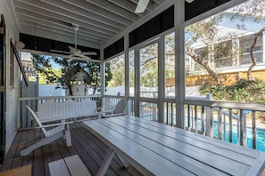 A covered outdoor seating area with a wooden deck, white chairs, and a ceiling fan. - Pet Friendly w/ Pool Near Beach & Seaside- Tupelo Honey by Royal Destinations (Santa Rosa Beach)