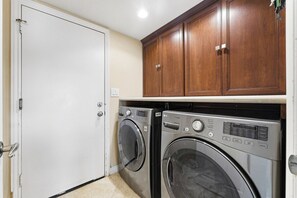 A laundry room with two front-loading washing machines, wooden cabinets above, and a white door. - Classic California Retreat (Laguna Niguel)
