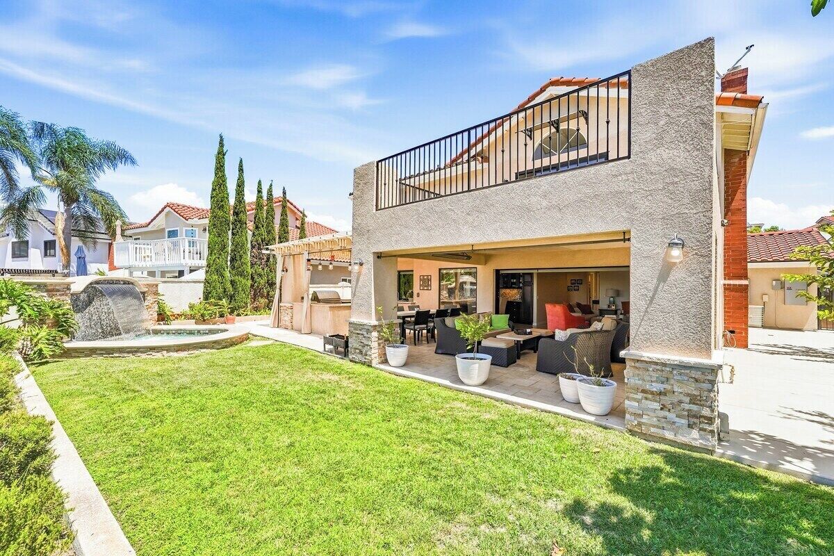 Una casa de dos pisos con balcón, zona de estar al aire libre y piscina.