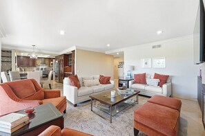 Ein modernes Wohnzimmer mit zwei Sofas, einem Couchtisch und einem Essbereich, im Hintergrund ist eine Küche erkennbar.