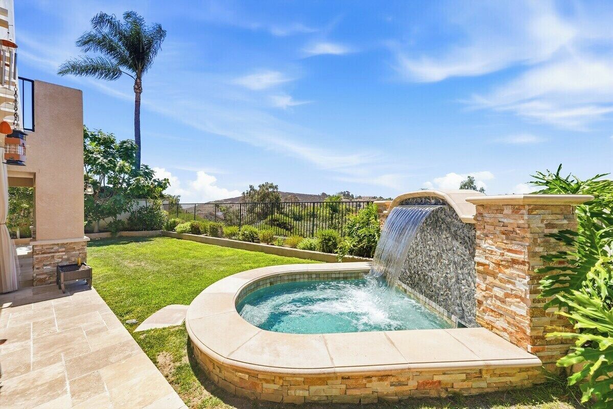 A backyard with a hot tub, a waterfall feature, and a well-maintained lawn.
