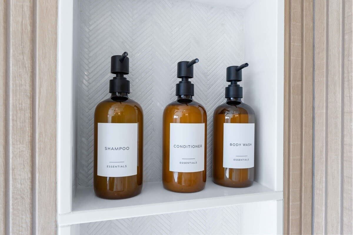 Tre flasker shampoo, conditioner og shower gel på en hvid hylde.