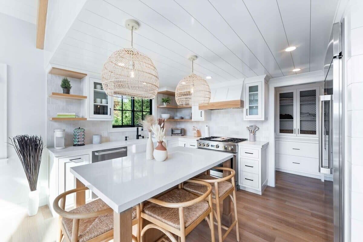 Una cocina moderna con armarios blancos, una isla grande, sillas de mimbre e iluminación colgante.
