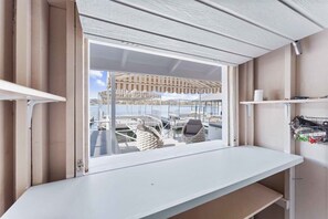 Una habitación con un ventanal grande, un escritorio blanco y vistas a barcos y un puerto deportivo.