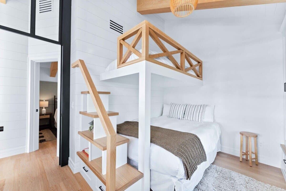 Ein Schlafzimmer mit einer Holztreppe, einem Bett mit weißer Bettwäsche und einem kleinen Hocker.