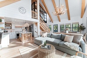 A spacious living area with a large sofa, a dining table, and a kitchen in the background. - Majestic Lakeview Lodge w/ Private Dock (Lake Arrowhead)