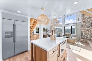 A modern kitchen with a large island, stainless steel refrigerator, and a stone accent wall. - Majestic Lakeview Lodge w/ Private Dock (Lake Arrowhead)