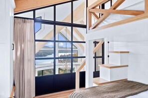 A modern room with a large window, a wooden ceiling structure, and a view of a body of water. - Majestic Lakeview Lodge w/ Private Dock (Lake Arrowhead)