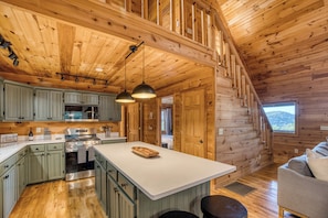 A cabin interior with a kitchen, dining area, and a staircase leading to a loft. - Thoughtfully updated cabin with mountain views, screened decks, hot tub (Blue Ridge)