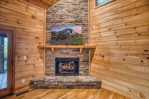 Interior de una cabaña de troncos con chimenea de piedra, paredes de madera y un cuadro colgado de un tren.
