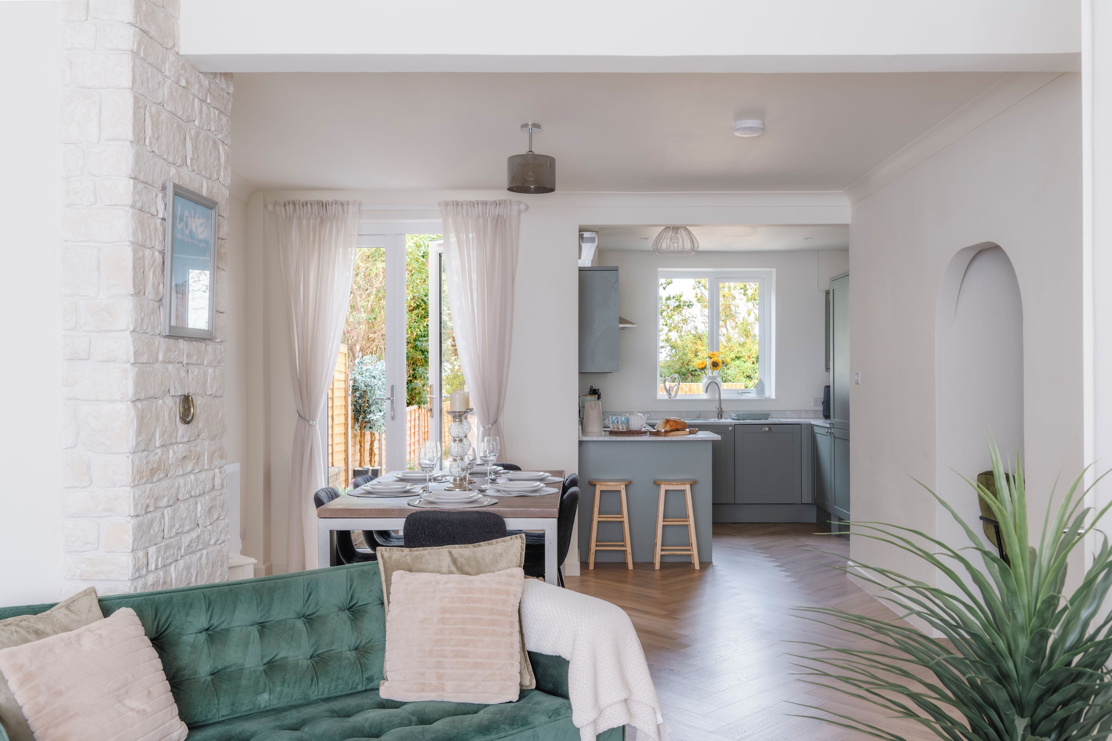 Un salon moderne avec un canapé vert, une table à manger dressée pour quatre personnes et une cuisine en arrière-plan.